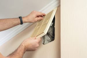 Technician's hands removing a wall vent cover to reveal dusty ductwork during a home air quality inspection in Central Florida.