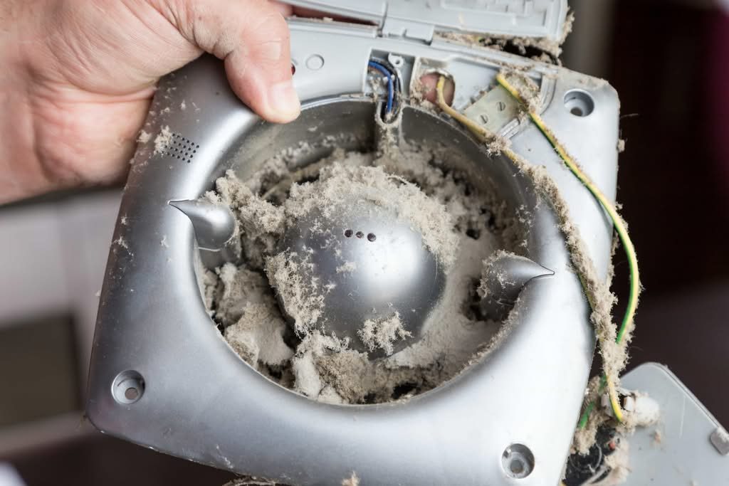 Why May is the Best Month for Professional Dryer Vent Cleaning 2 Close-up of a technician's hands holding a heavily dusty silver exhaust fan during a professional ventilation cleaning service in Ocala, Florida.