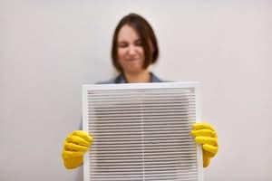 Technician in yellow gloves holding a dusty white ventilation grille during an indoor air quality inspection in Central Florida.