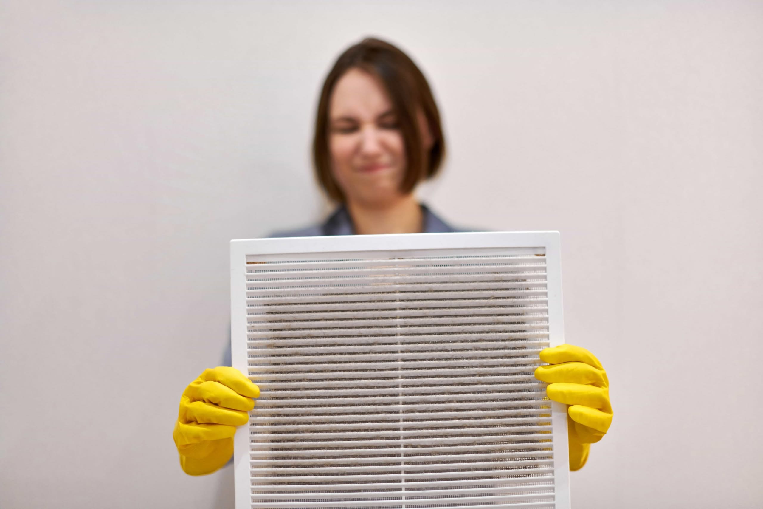 Why May is the Best Month for Professional Dryer Vent Cleaning 1 Technician in yellow gloves holding a dusty white ventilation grille during an indoor air quality inspection in Central Florida.