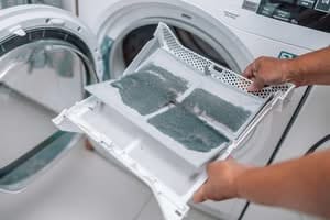 Close-up of a person's hands holding a white plastic dryer lint trap heavily covered in a thick layer of grey dust and fabric debris in front of an open dryer door for condo and townhome dryer vent cleaning.