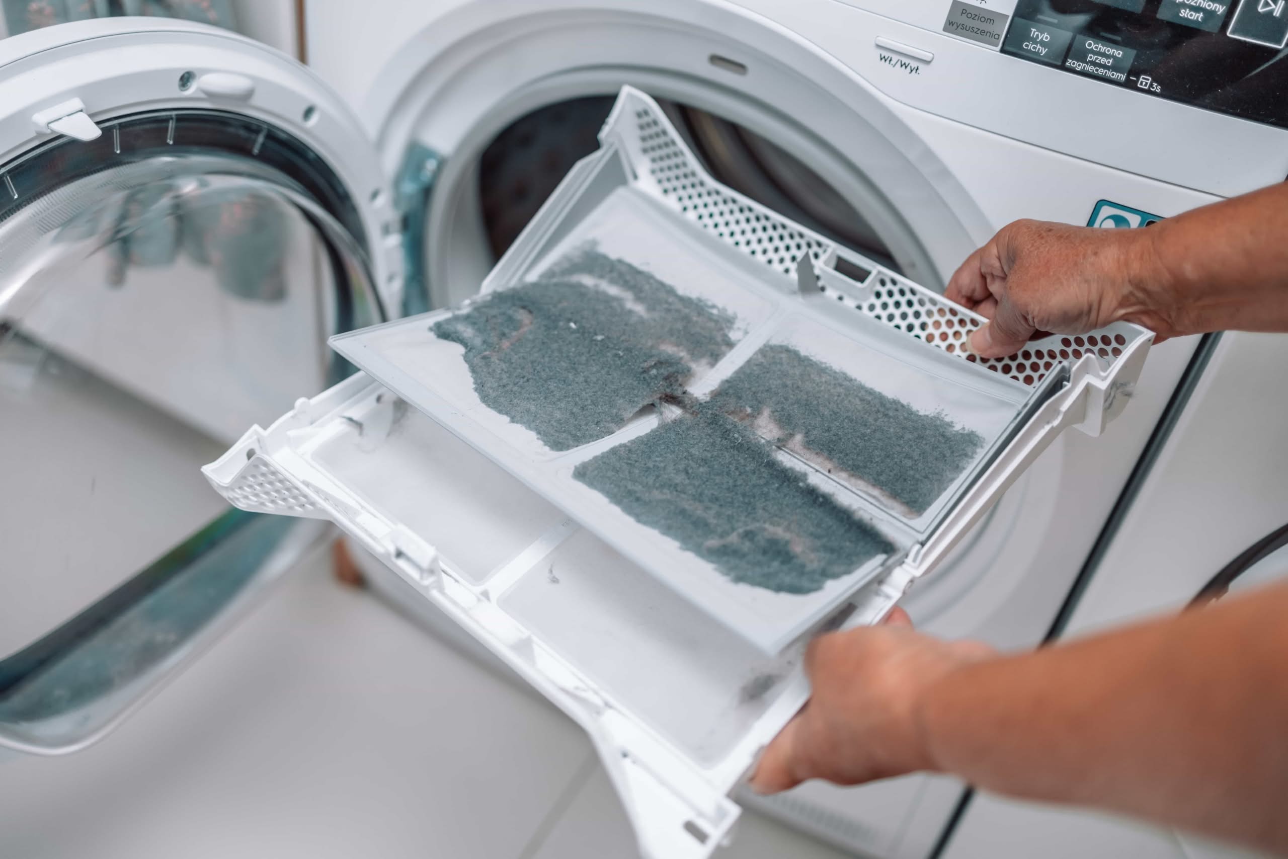 Condo and Townhome Dryer Vent Cleaning Clermont: Ultimate Expert Guide 1 Close-up of a person's hands holding a white plastic dryer lint trap heavily covered in a thick layer of grey dust and fabric debris in front of an open dryer door.