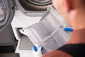 Technician in work gloves removing a heavily clogged lint screen during an internal dryer cabinet cleaning in Central Florida.