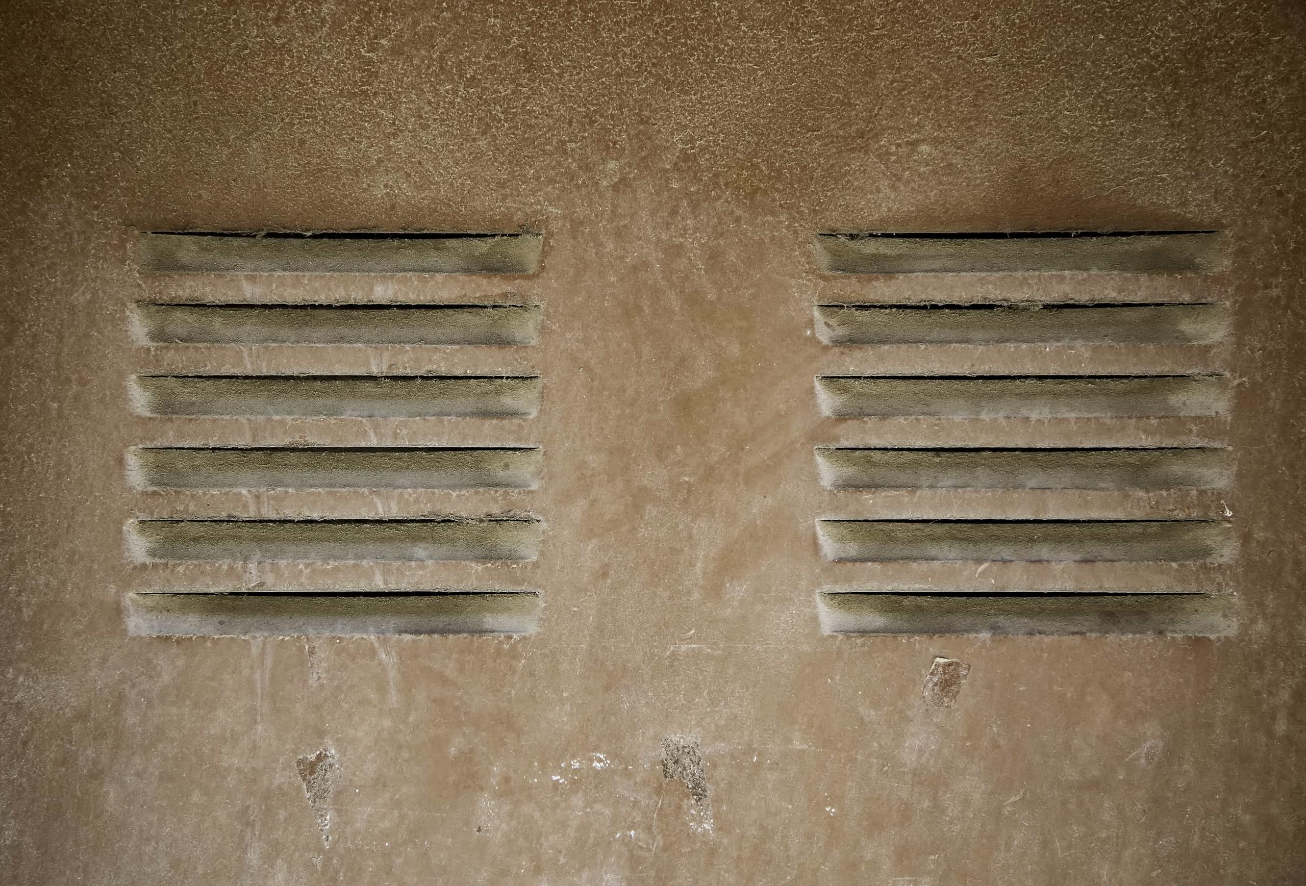 Older Dryer Vents: Hidden Fire Hazards in The Villages 1 A close-up view of two older dryer vents built into a textured, dusty beige exterior stucco wall in Las Vegas, Nevada, showing accumulated dirt around the slats.