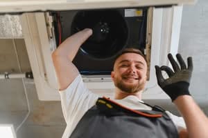 A smiling HVAC technician working inside a ceiling ventilation unit and making an OK sign, illustrating professional dryer vent cleaning and air duct safety services in Phoenix, Arizona.