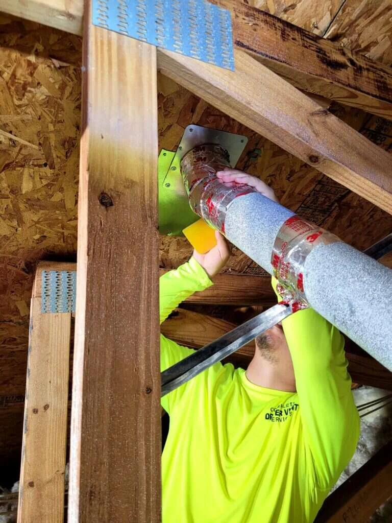technician applying dryer duct sealing tape at a metal joint in an attic